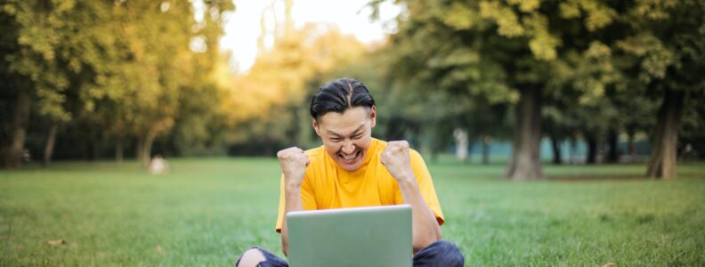 Happy man sitting on grass with laptop on his lap